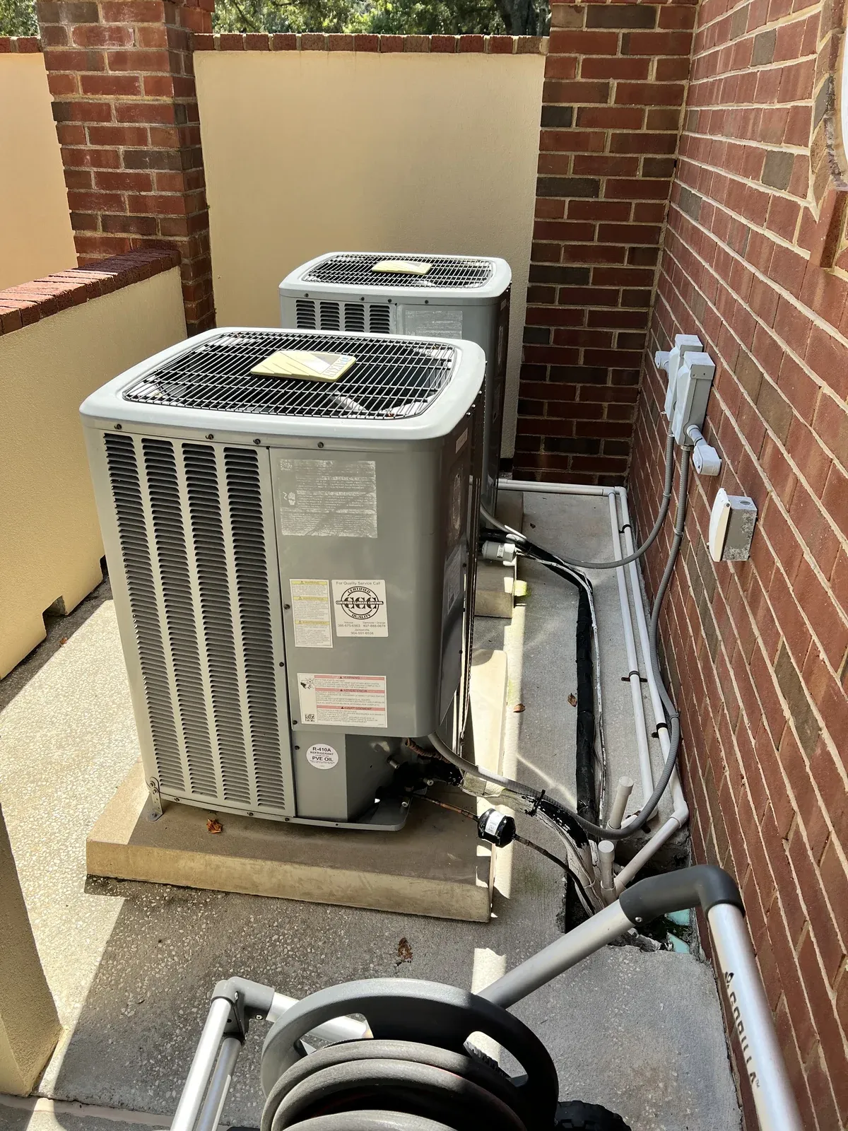 Two outdoor air conditioning condensers installed beside a brick home